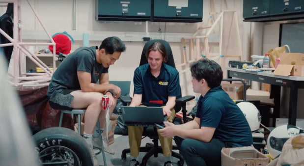 Three students collaborating on a project in a workshop for Formula SAE, focusing on design and engineering.