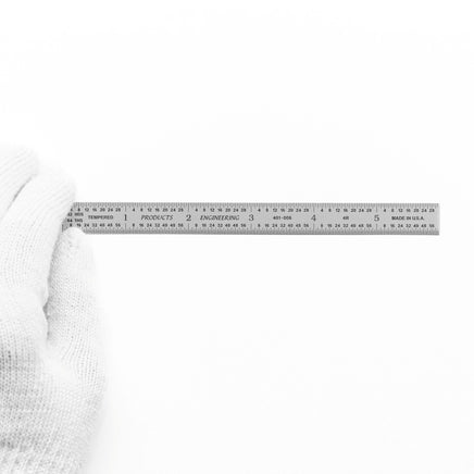 Hand holding a chrome-plated steel ruler against a white background, showcasing its precise graduations.