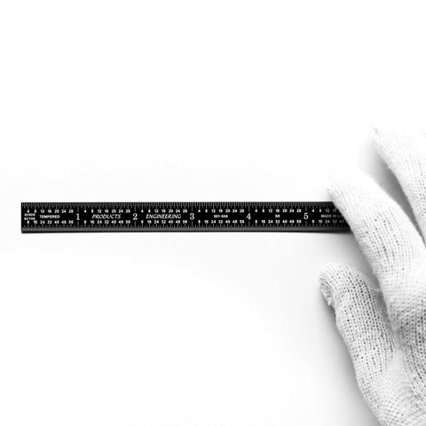 Black chrome flexible rulers placed on a white background with a gloved hand, showcasing precise etching and readability.